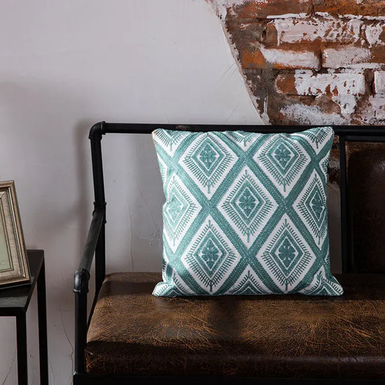 Geometric teal throw pillow on rustic brown leather bench by exposed brick wall