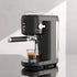Modern black espresso machine brewing coffee into a glass cup on a kitchen counter