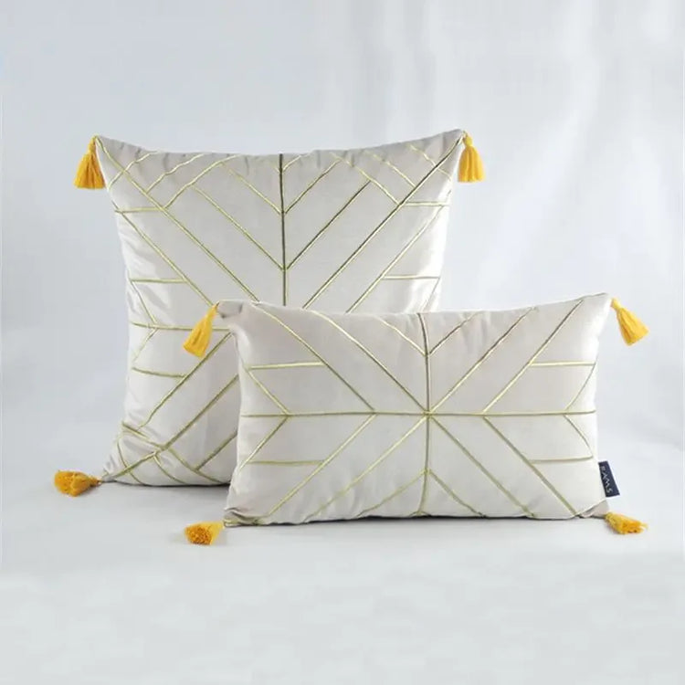 White decorative pillows with gold geometric lines and yellow tassels on a light background