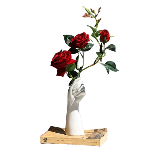 Ceramic hand vase with red roses on a book, displayed on a white round table
