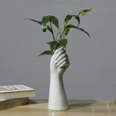 White ceramic hand vase holding green plant on wooden desk with books