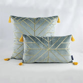 Velvet throw pillows with gold geometric lines and yellow tassels on a plain backdrop