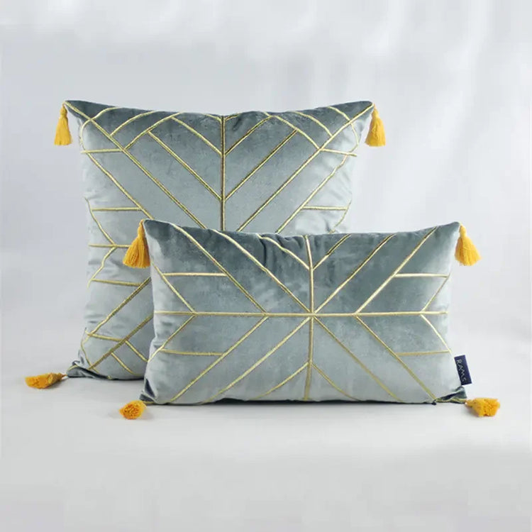 Velvet throw pillows with gold geometric lines and yellow tassels on a plain backdrop
