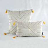 Set of two white decorative pillows with gold geometric lines and yellow tassels on corners