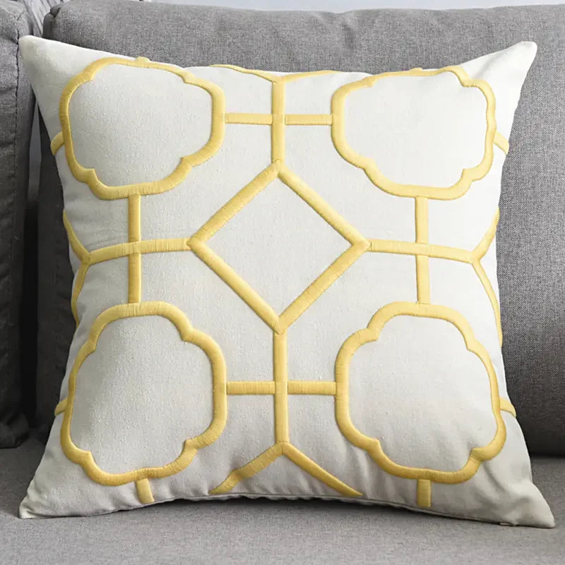 Yellow geometric embroidered throw pillow on a gray sofa