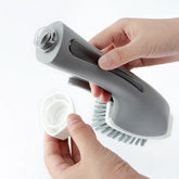 Hands assembling a gray dish brush with soap dispenser on a white background