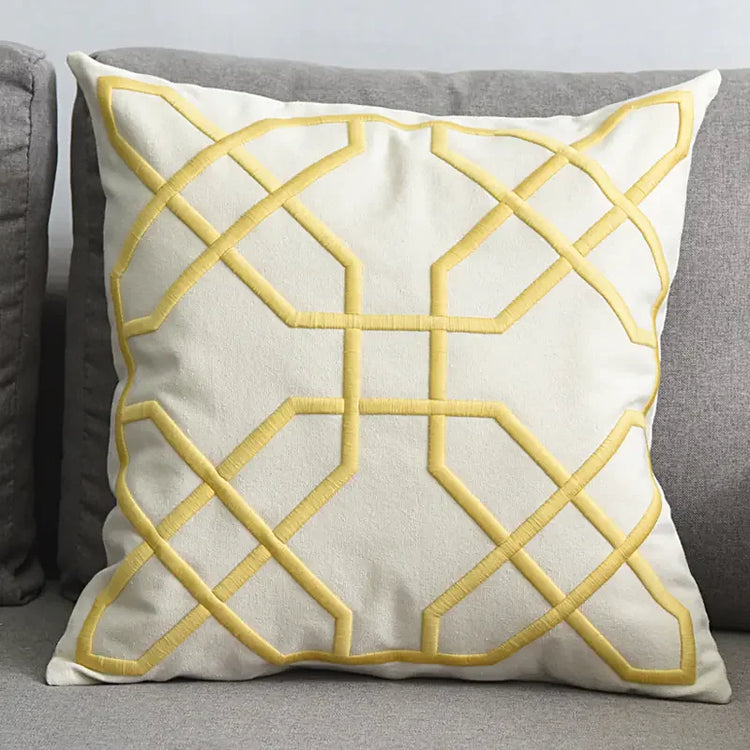 Cream decorative throw pillow with yellow geometric embroidery on a grey sofa
