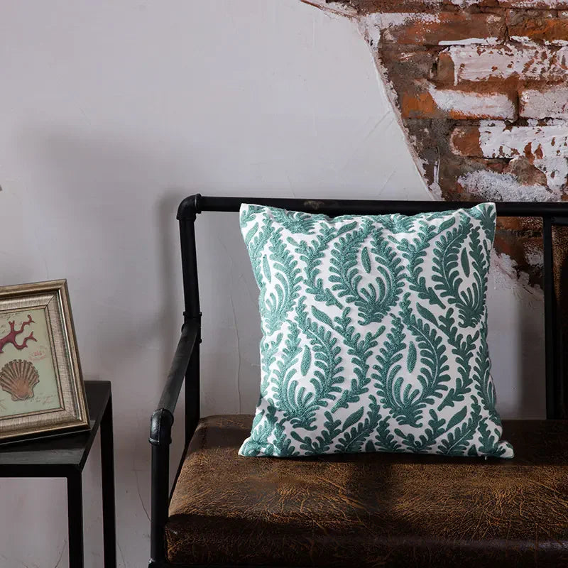 Decorative green leaf pattern pillow on brown bench against rustic brick wall