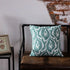 Decorative green leaf pattern pillow on brown bench against rustic brick wall