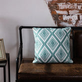 Geometric teal throw pillow on rustic brown leather bench by exposed brick wall