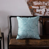 Blue geometric throw pillow on brown leather bench against rustic brick wall