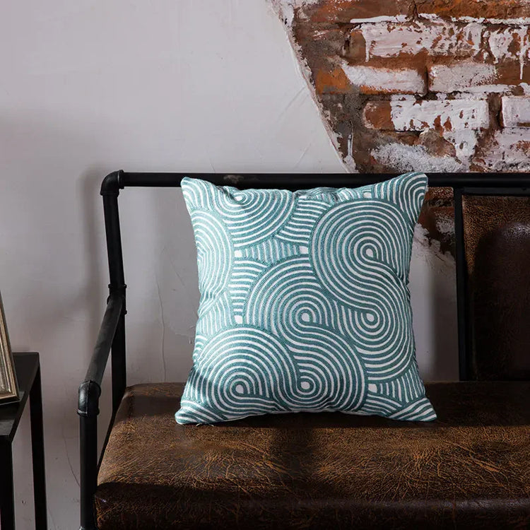 Blue geometric throw pillow on brown leather bench against rustic brick wall