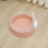 Pink plastic cat litter box with scooper on light wooden floor
