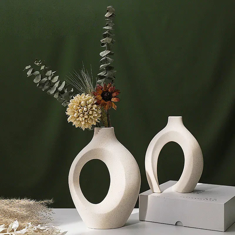 Modern ceramic open vases with dried flowers on white table, green background, minimalist decor