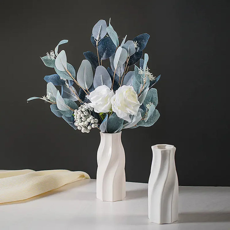 Modern white ceramic vase with artificial eucalyptus and white roses on a gray background