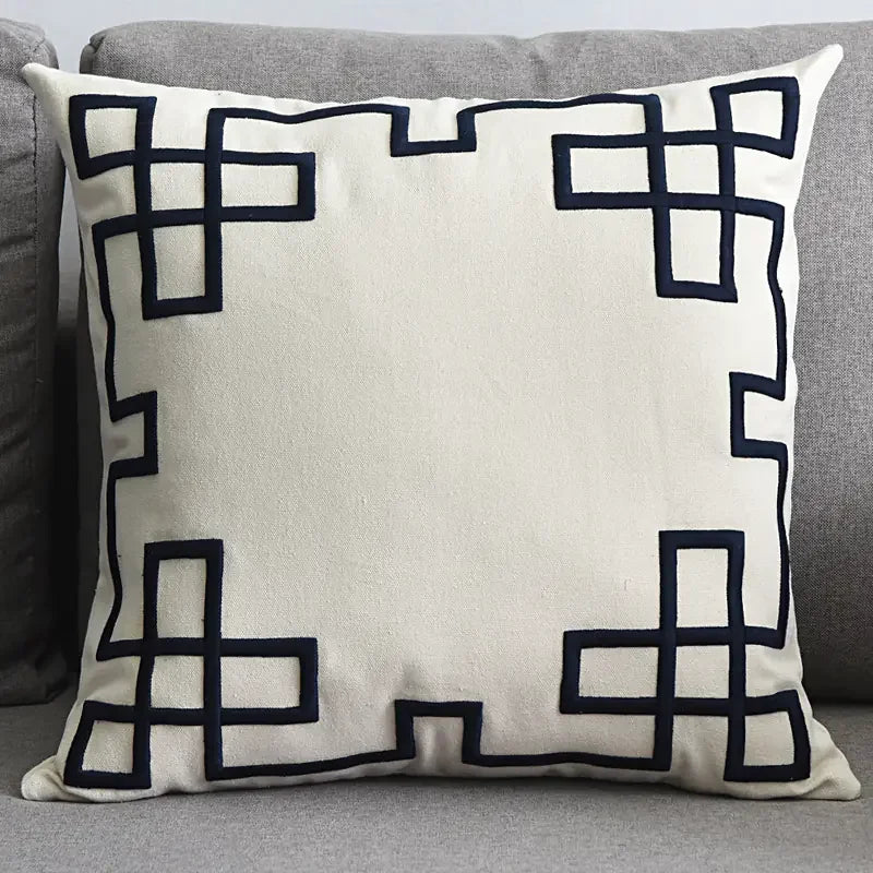 Modern beige throw pillow with black geometric border on a grey sofa