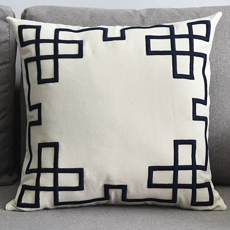 Modern beige throw pillow with black geometric border on a grey sofa