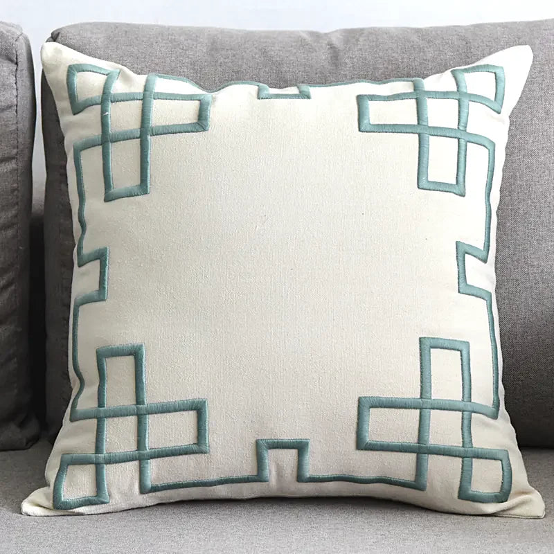 Modern cream throw pillow with teal geometric embroidery on a gray sofa