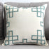 Modern cream throw pillow with teal geometric embroidery on a gray sofa